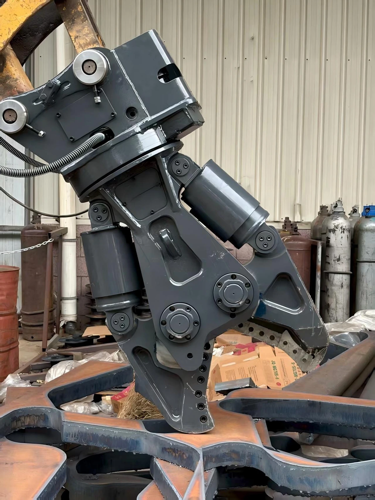 Angled workshop view of a hydraulic shear hanging from an excavator arm