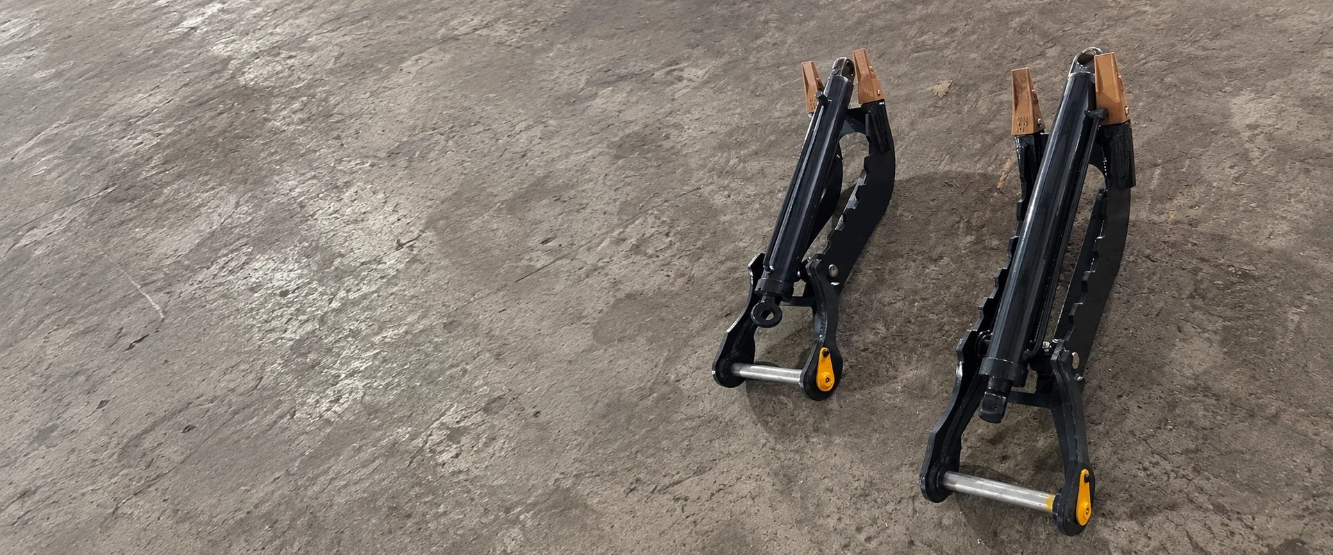 Two black hydraulic thumbs upright side by side on their original workshop floor, showing cylinders and pins