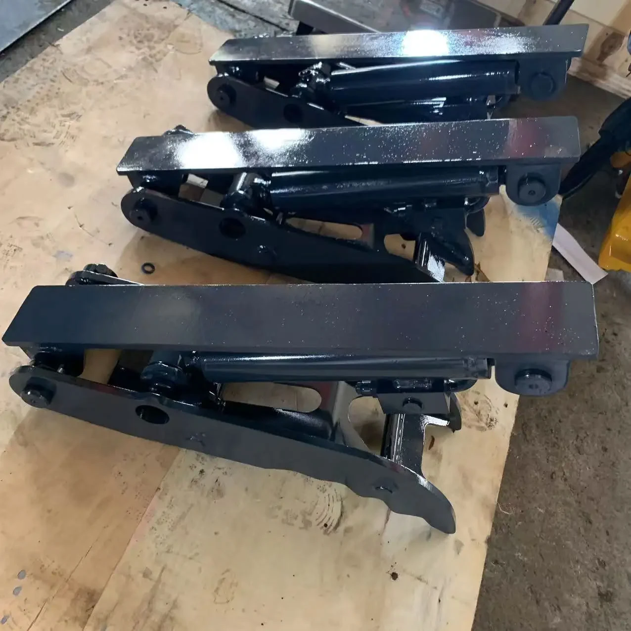 Two black hydraulic thumb assemblies laid on a workshop pallet