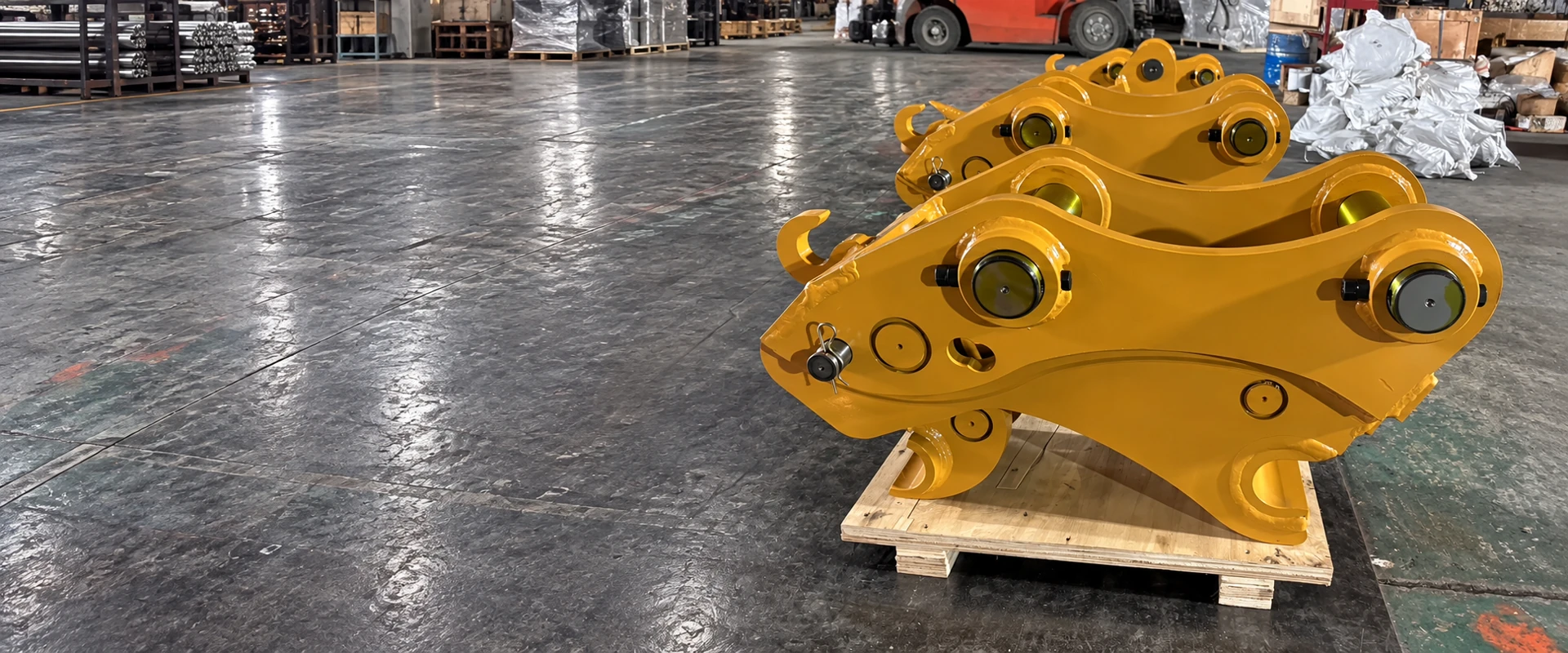 Yellow quick coupler in a workshop, showing side plates, two pins and attachment connection