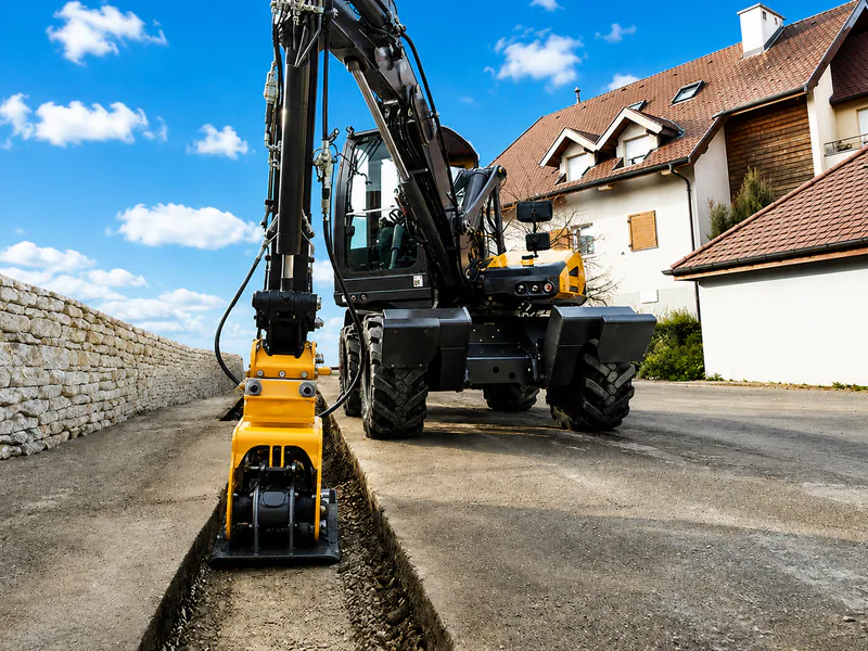 Excavator plate compactor working beside a paved edge