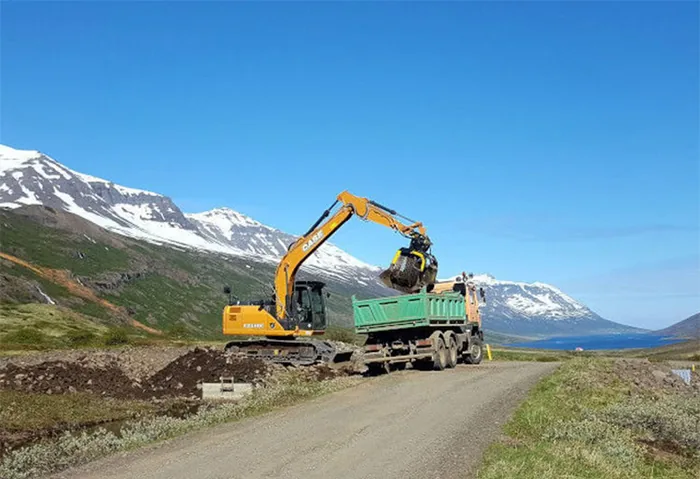 Excavator with a Screening Bucket loading material beside a mountain road